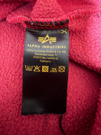 Just Casual Alpha Industries Sweatshirt Pflegeetikett mit Logo und Waschanleitung auf rotem, angerautem Stoff