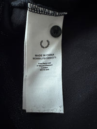 Just Casual Fred Perry Poloshirt Pflegeetikett mit Lorbeerkranz-Logo und Herstellungsdetails auf schwarzem Stoff